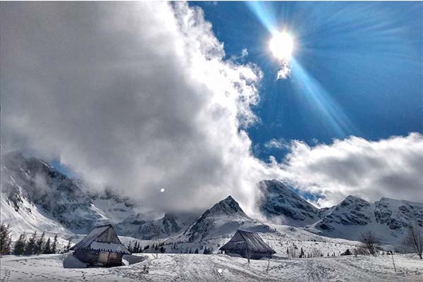 widok na halę gąsienicową zimą, widać domki w śniegu i słońce zza chmur