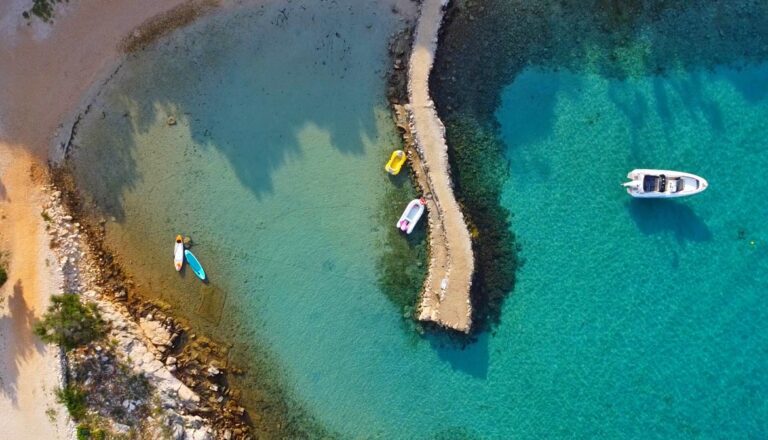 widok z drona na fragment plaży i morza. widać turkusowe morze, brzeg, zakotwiczona łódkę i dwa sumy